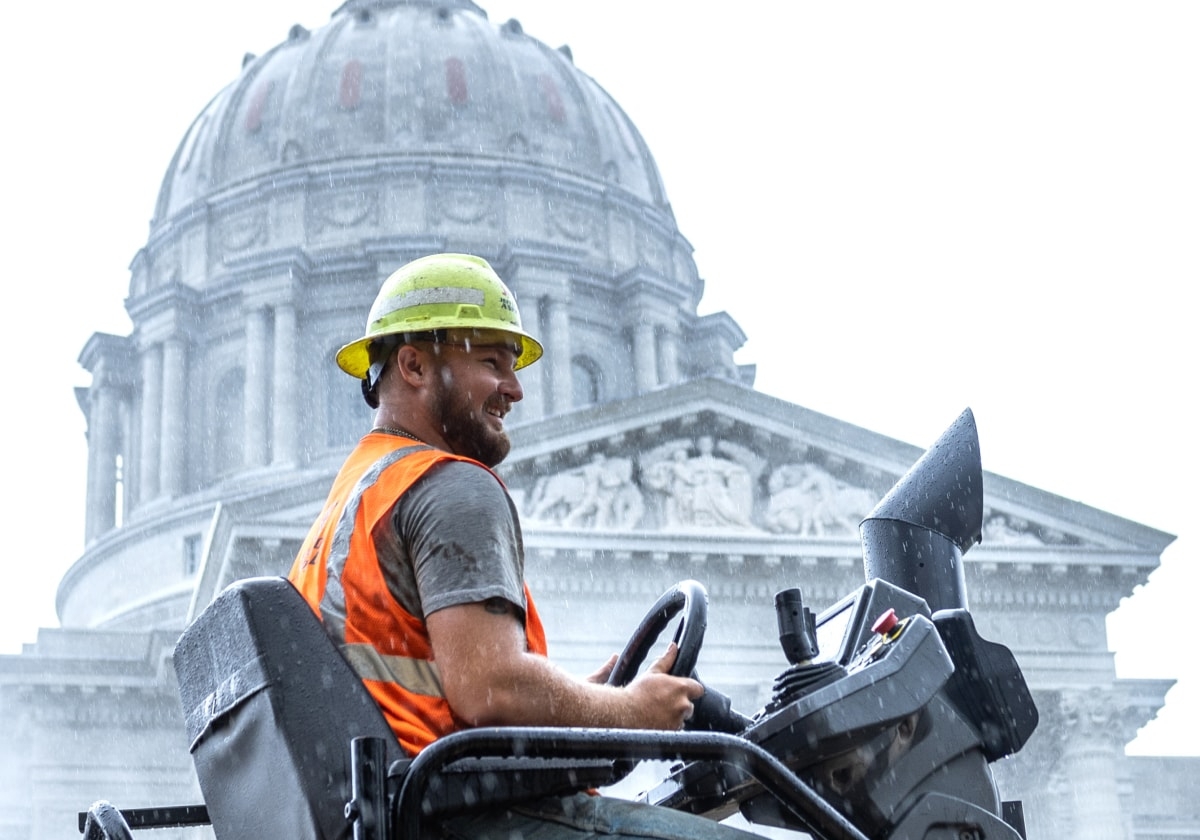 Paving crew worker on paving truck in front of Missouri Capital building